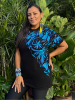 Woman wearing a black t-shirt with blue floral patterns standing in front of green foliage.