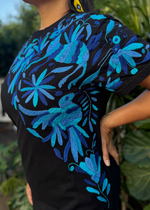 Person wearing a black t-shirt with blue floral patterns against a blurred green background