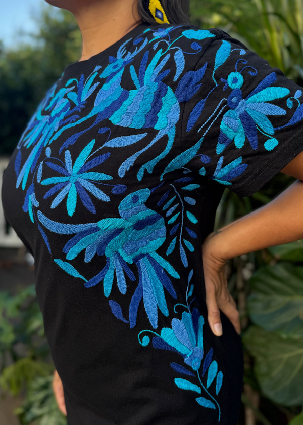 Person wearing a black t-shirt with blue floral patterns against a blurred green background