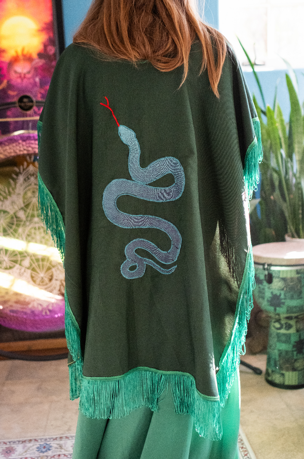 Hand-embroidered deep green ceremonial poncho with sky-blue serpent motif and lush fringe, designed as a 1-of-1 ritual cloak for transformation and spiritual presence.