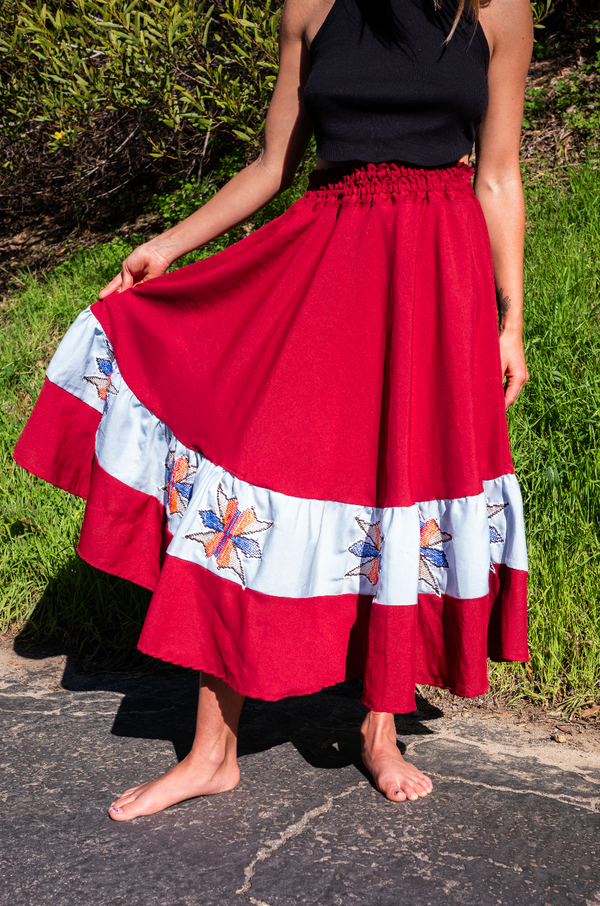 Deep red hand-embroidered ceremonial skirts with black Thunderbird and star blossom motifs, crafted by Amazonian artisans to honor indigenous spirit and sacred movement.